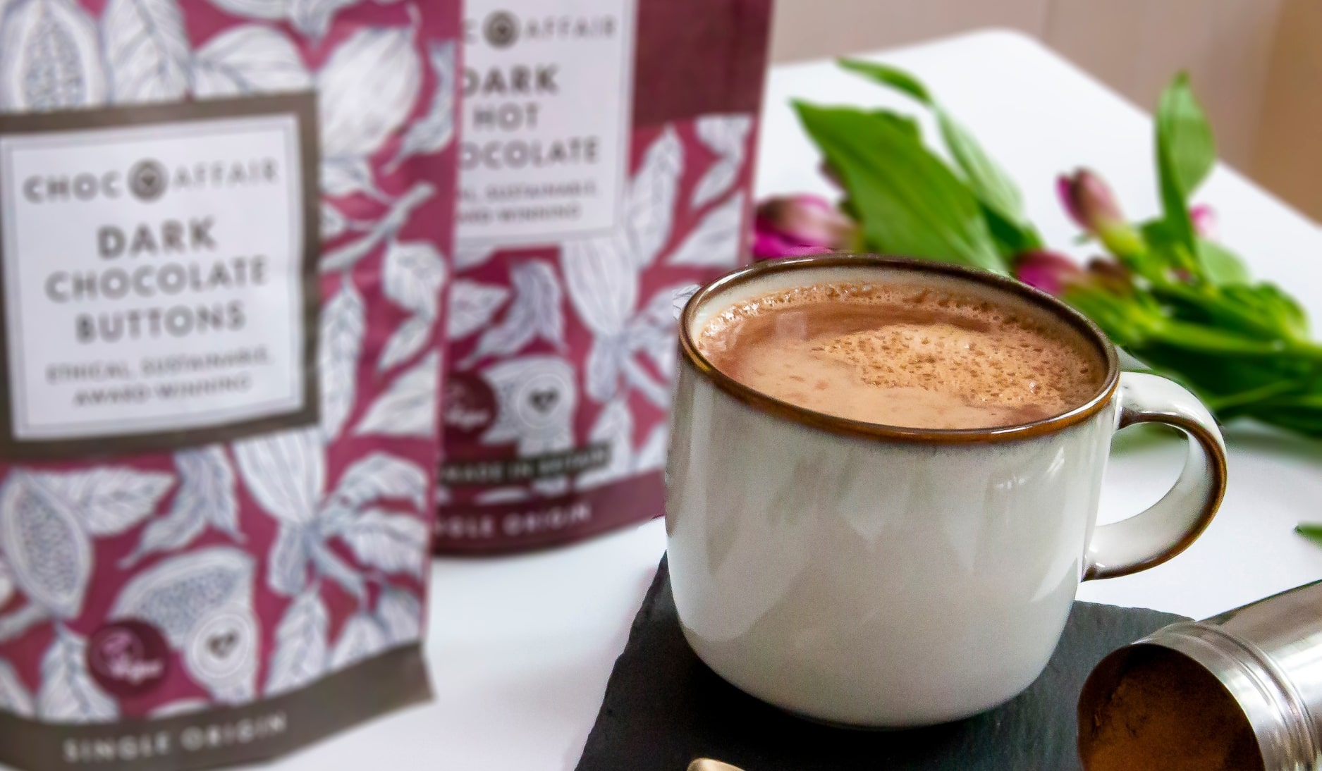 A mug of hot chocolate next to a bag of dark chocolate buttons