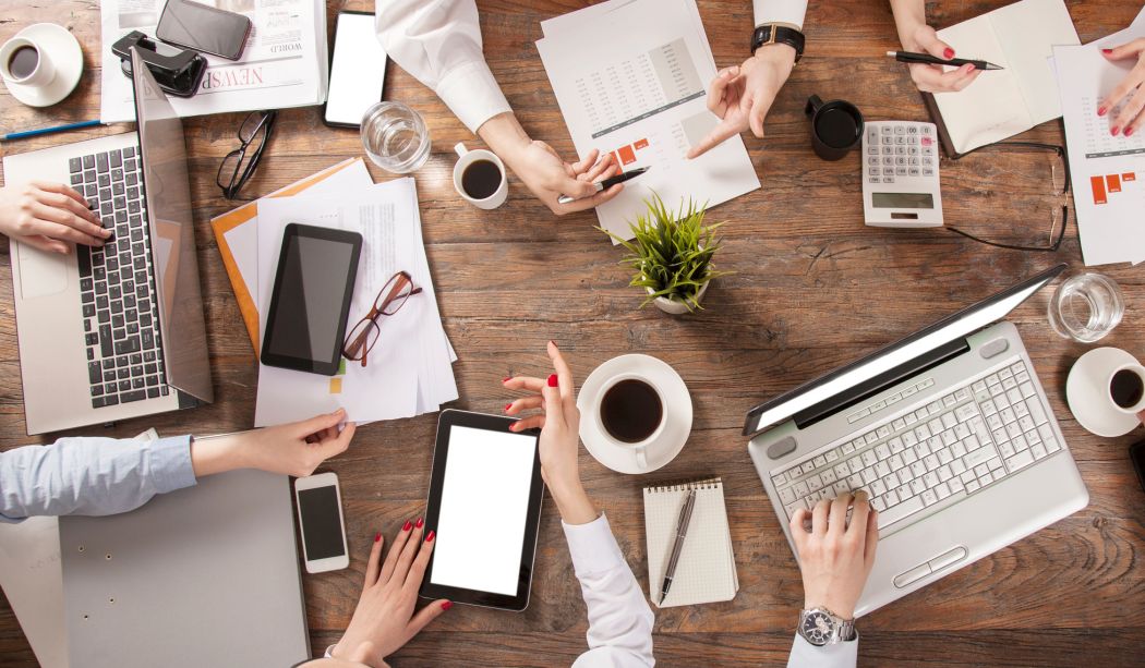 Birds-eye photo of a meeting with laptops and paper